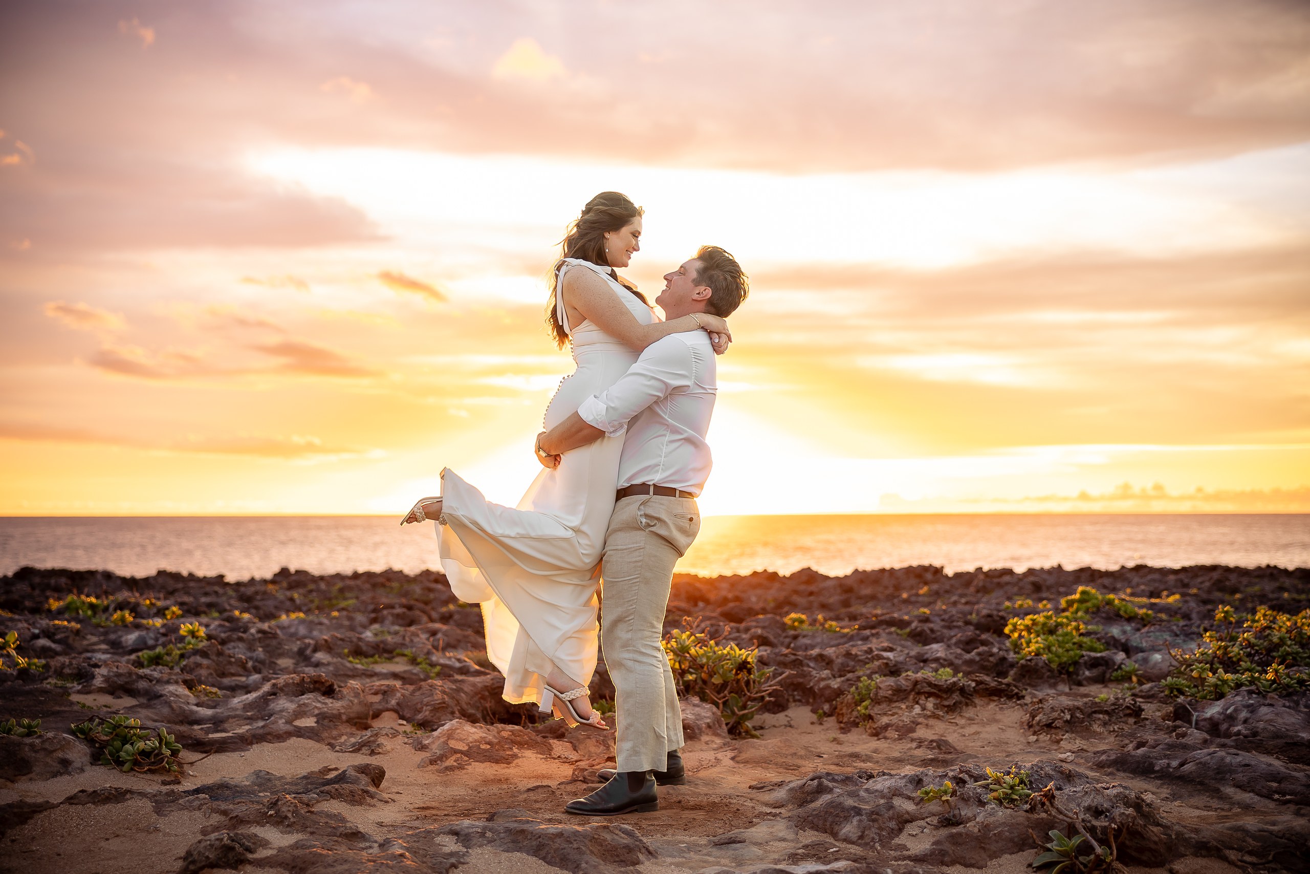 Groom lifting the bride against an orange and pink sunset