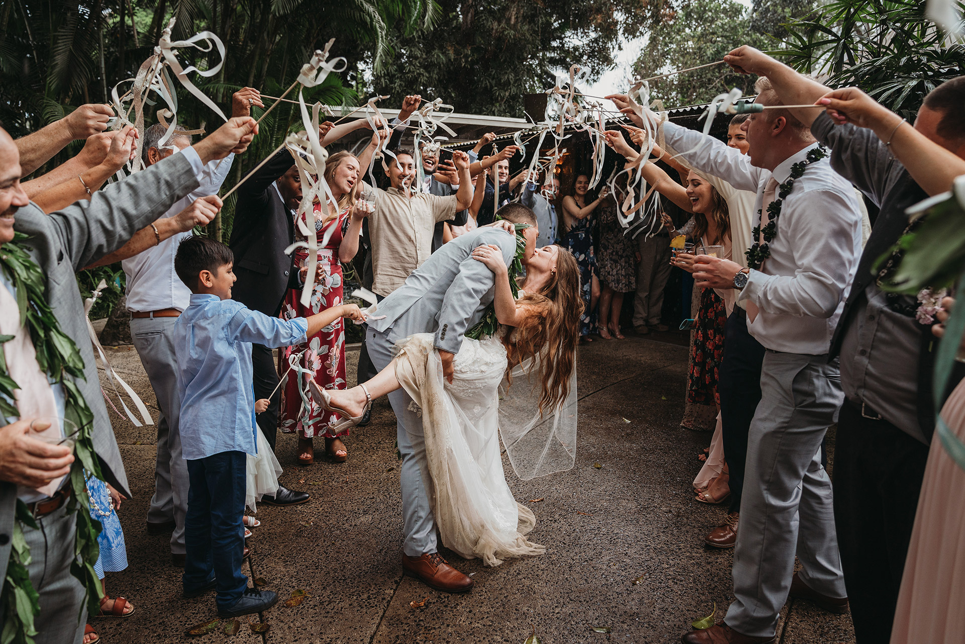 A newlywed couple kisses beneath ribbons waved by their guests